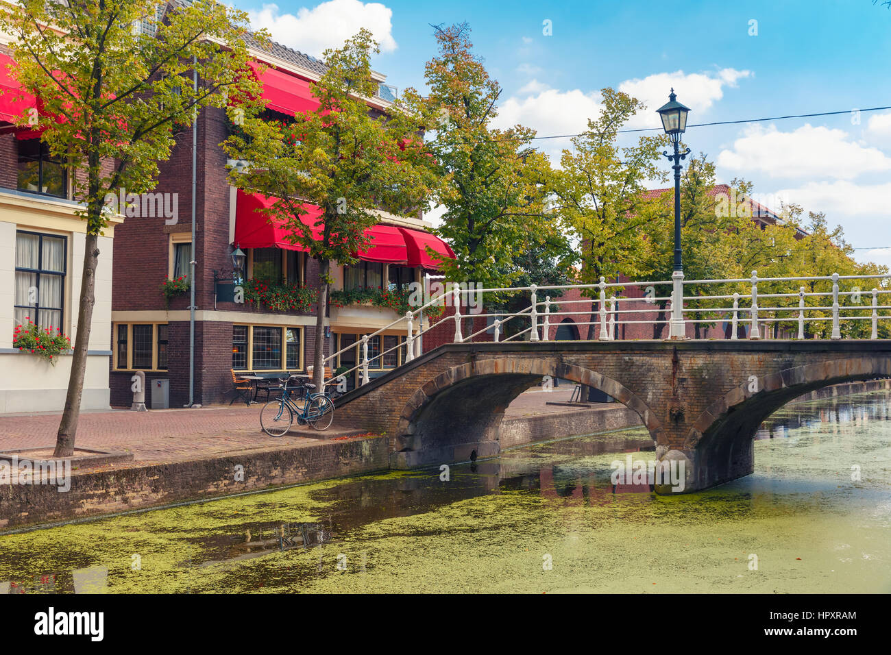 Die malerische Brücke mit einer Laterne durch den Kanal und typische Häuser an einem sonnigen Tag in Delft, Zuid-Holland, Niederlande. Stockfoto