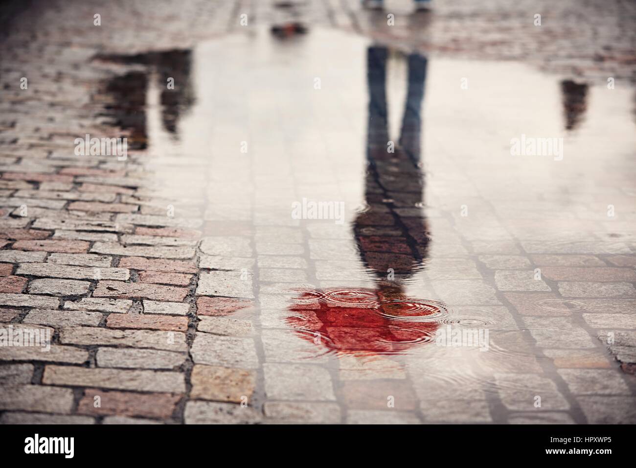 Regnerischen Tag. Reflexion der junger Mann mit roten Regenschirm in Pfütze auf der Stadtstraße bei Regen. Stockfoto