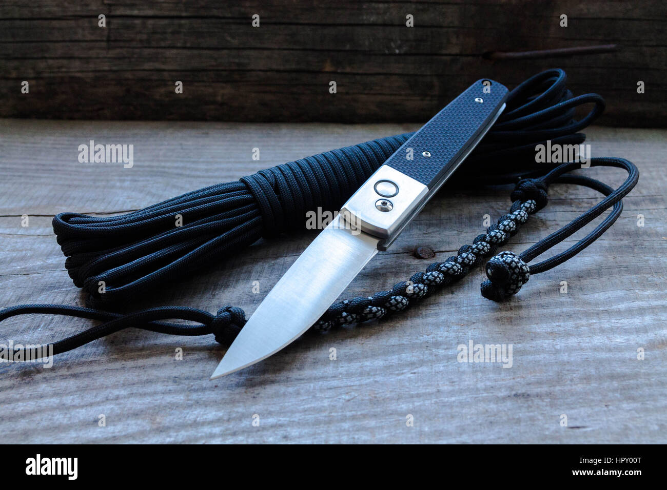 Switchblade Messer und einem schwarzen Seil. Fallschirmschnur und Holz. Stockfoto