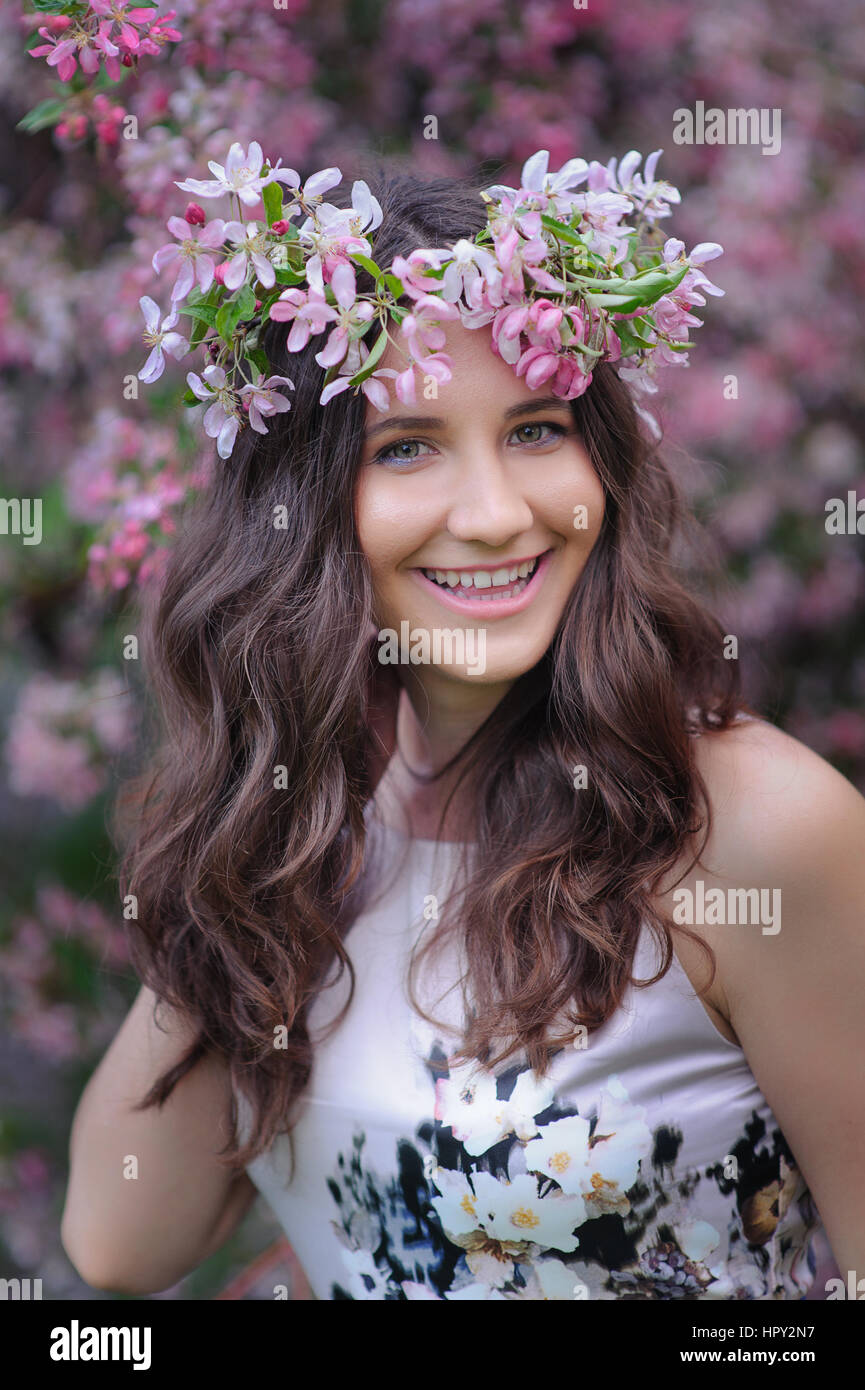 lächelnde junge Frau mit einem Kranz auf dem Kopf auf einem Hintergrund von Frühling Blütenbäumen. Stockfoto