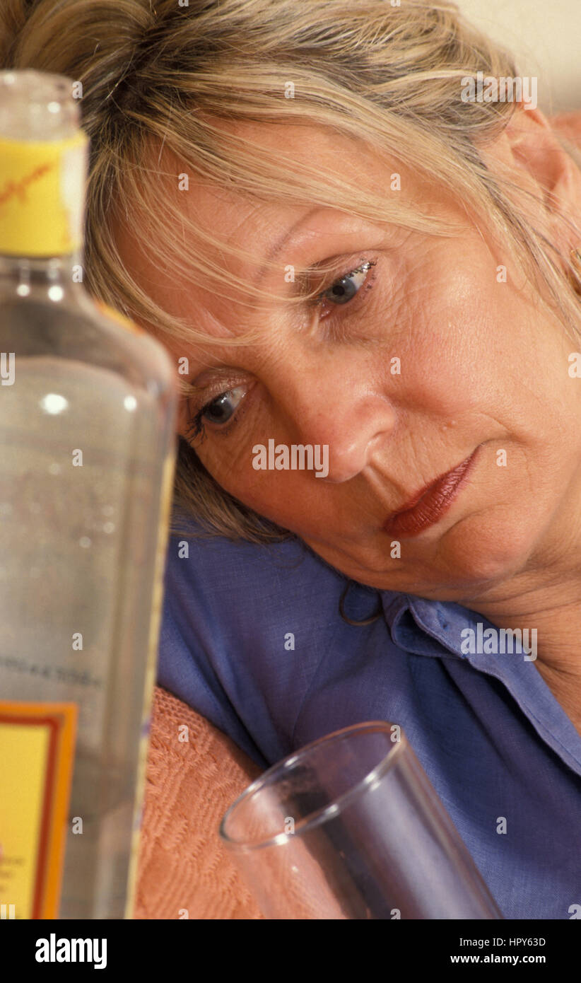 Unglücklich, reife Frau zusammengesunken neben Flasche Gin Stockfoto