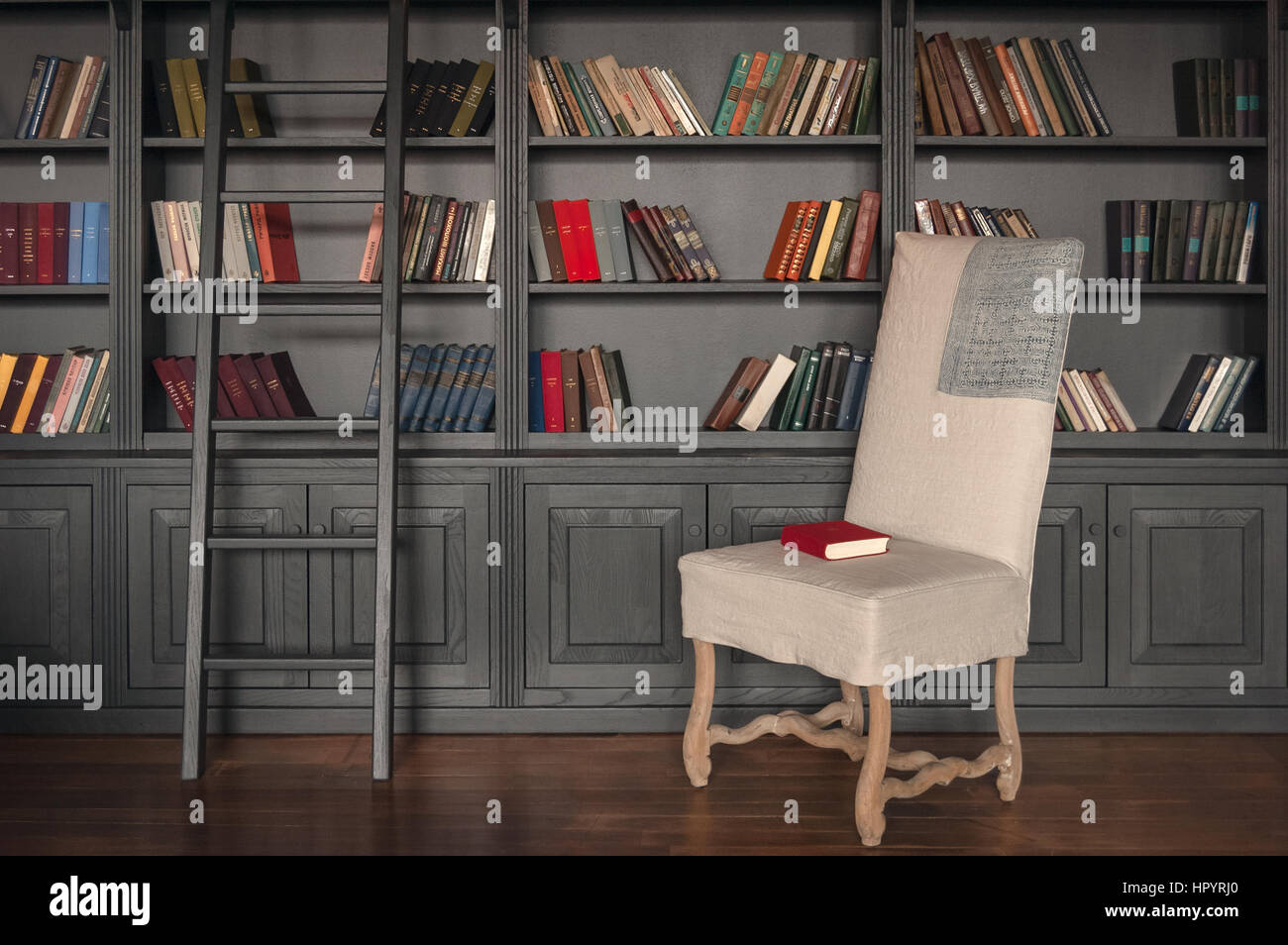 Home Bibliothekszimmer mit grauen Holzregal und farbigen Bücher in den Regalen, Holztreppen und weißen Stuhl mit roten Buch darüber. Stockfoto