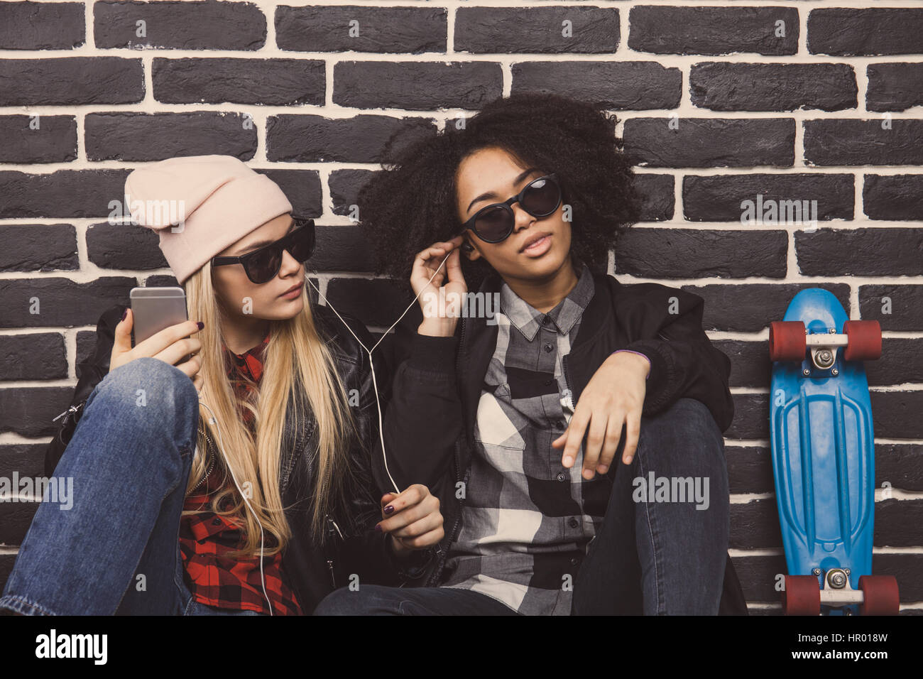 Lebensstil-Porträt von zwei beste Freunde Hipster Mädchen. Sie sitzen auf dem Betonboden vor einer schwarzen Wand und die Musik zu hören. Stockfoto