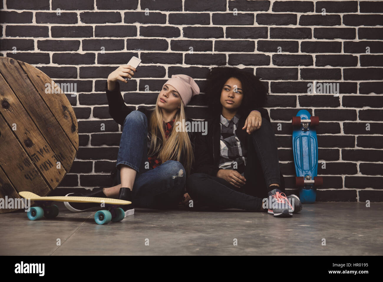 Lebensstil-Porträt von zwei beste Freunde Hipster Mädchen. Sie sitzen auf dem Betonboden vor einer schwarzen Wand und Selfie zu machen. Stockfoto