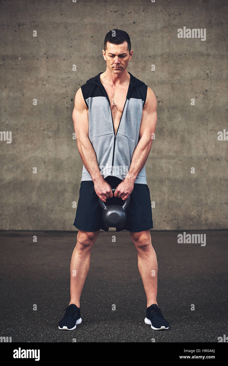 Starken Jüngling in Sportbekleidung Hintergrund Betonwand schwere Kettlebell festhalten. Stockfoto