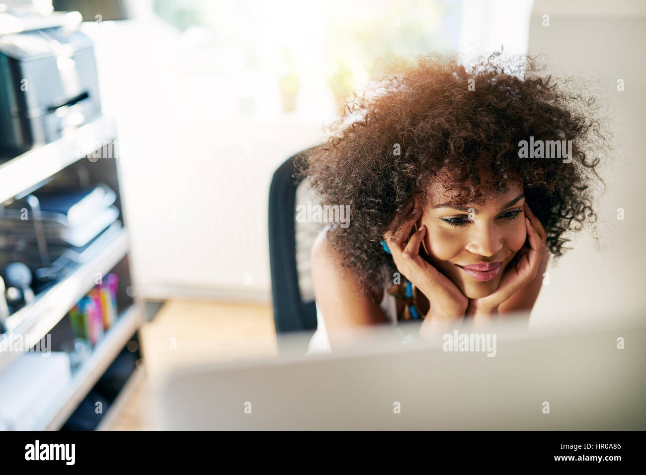 Junge hübsche afroamerikanischen Frau Blick auf Desktop-lächelnd auf im Hintergrund unscharf. Stockfoto