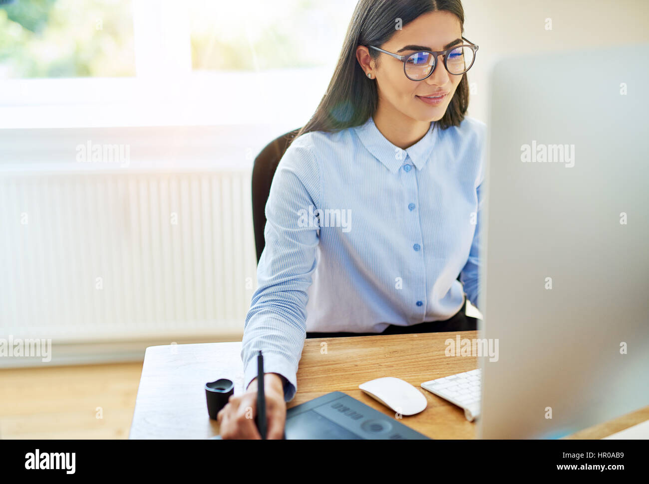 Digital Künstlerin in blauem Hemd und Brille arbeiten am Computer mit Stift und Tablett neben ihr auf Schreibtisch Stockfoto