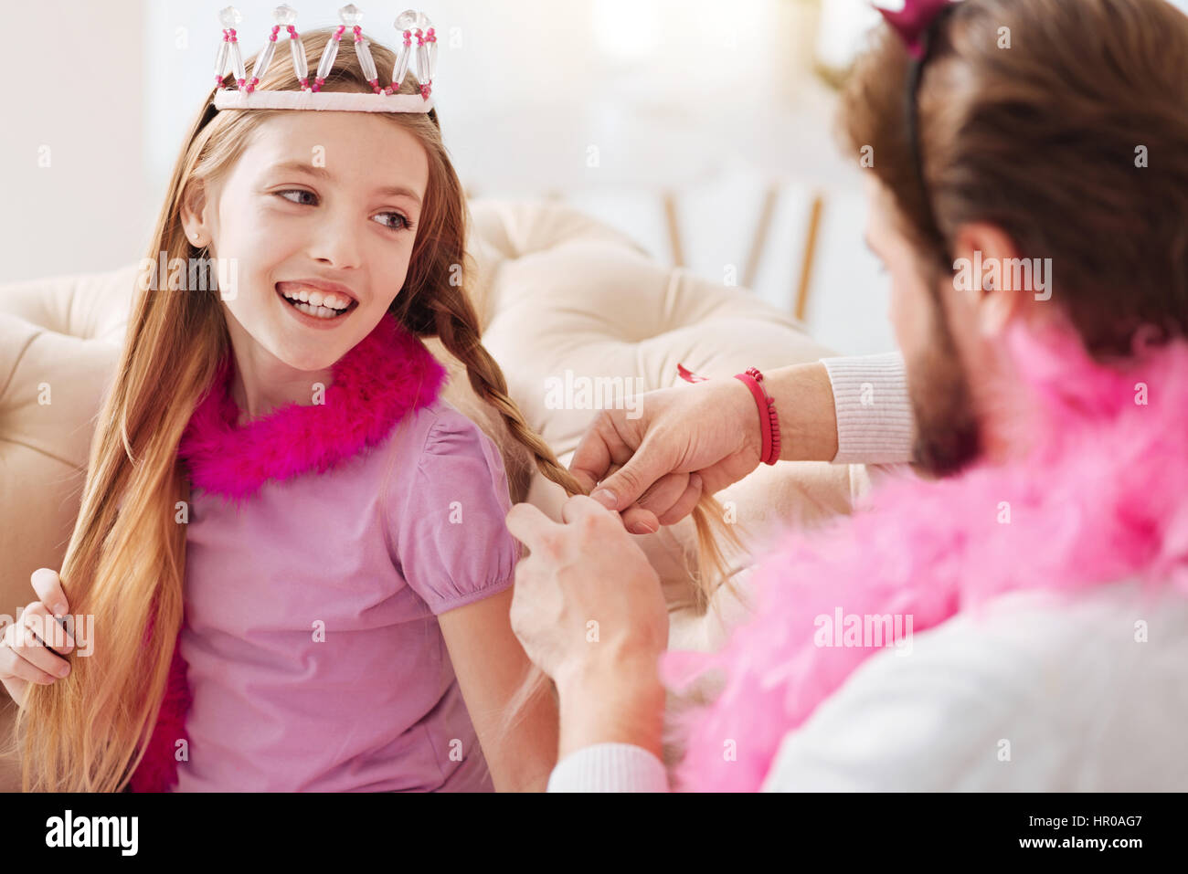 Neue Frisur. Attraktive langhaarige Mädchen mit rosa Feder um den Hals halten den Mund geöffnet, während Sie ihr Haar berühren Stockfoto