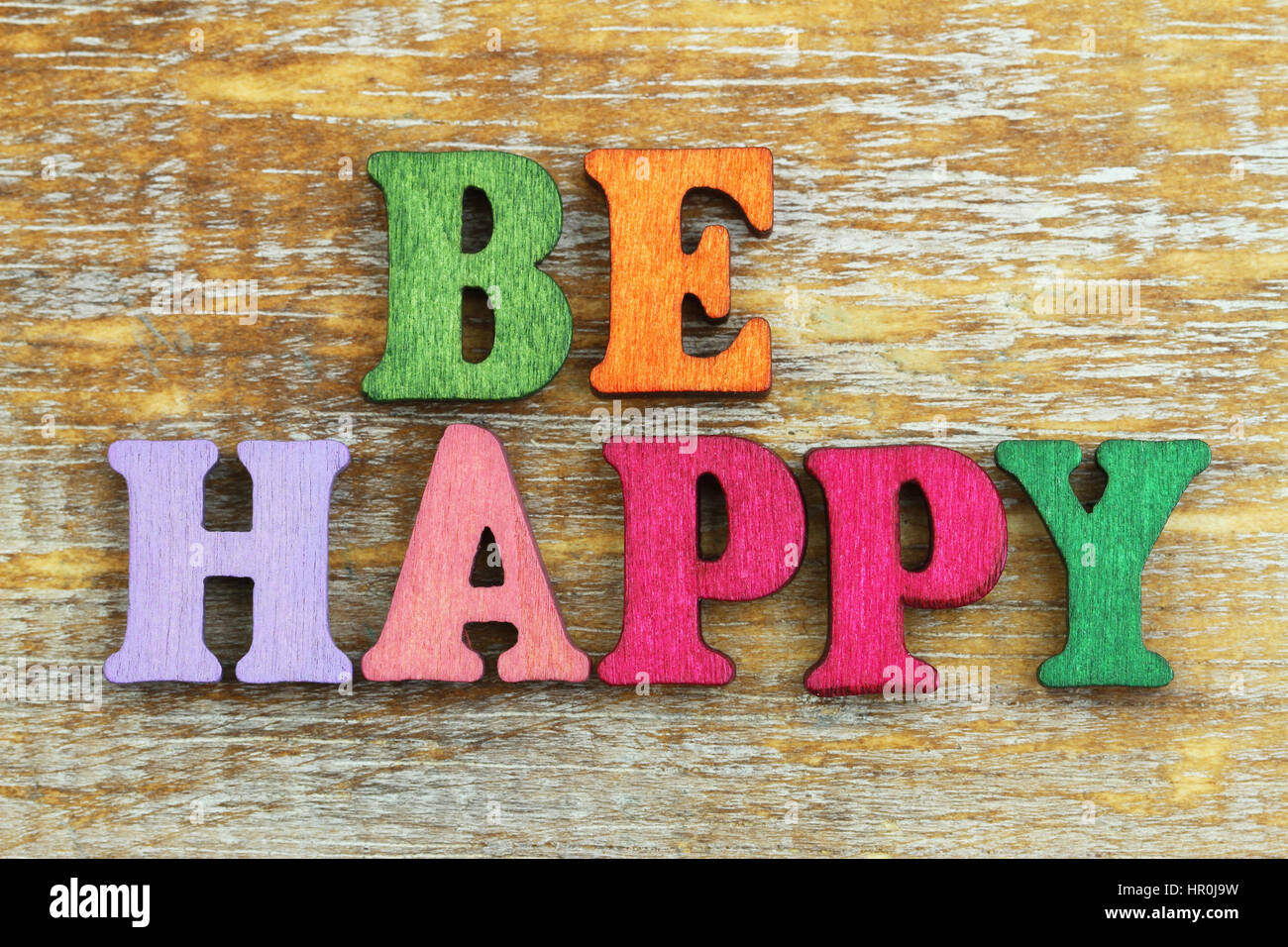 Glücklich sein mit bunten Buchstaben auf rustikalen Holzoberfläche geschrieben Stockfoto