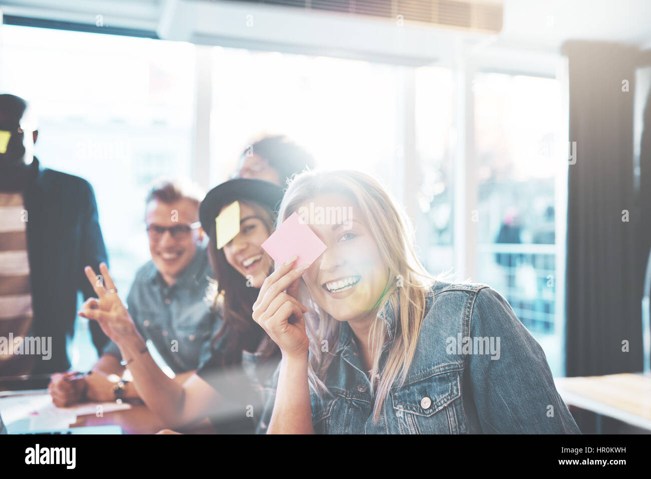 Schöne junge Menschen spielen Namensspiel, zwei Frauen und Männer posieren, Kamera gegen hellen Fenster mit Textfreiraum Stockfoto