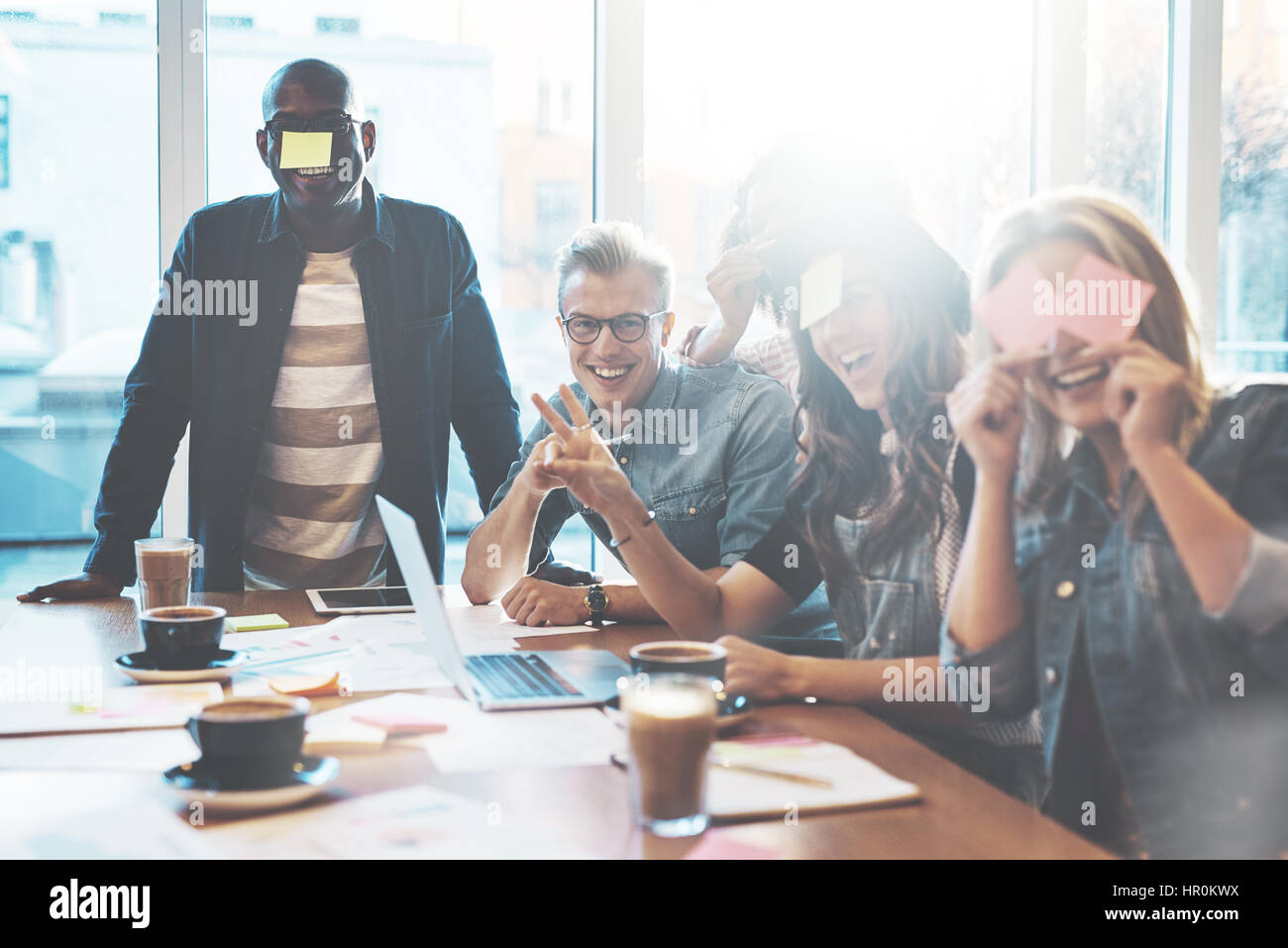 Gruppe von Jugendlichen im Café Spaß Spiel Name mit Haftnotizen auf ihre Stirn, gegen die großen hellen Fenster Stockfoto