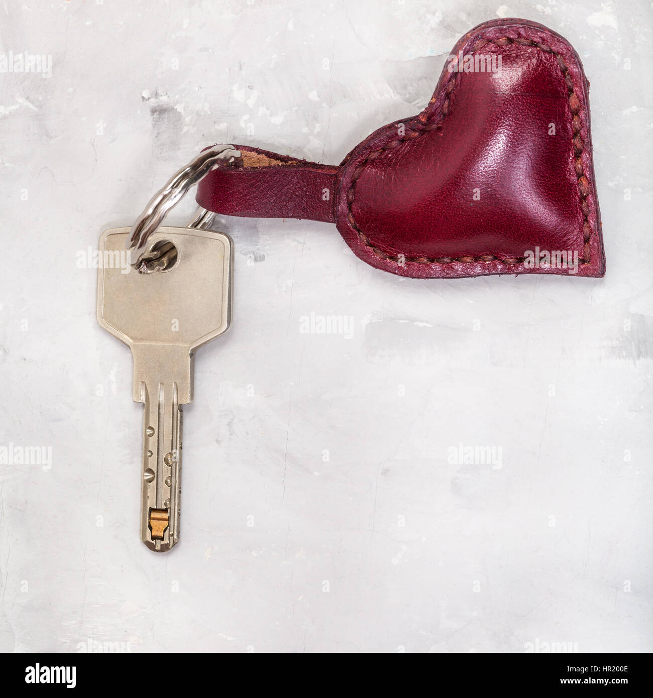 Türschlüssel mit rotem Leder Herz Form Schmuckstück auf Betonplatte Stockfoto