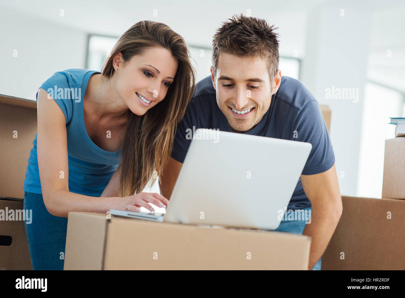 Glückliches Paar verbinden mit dem Internet mit einem Laptop in ihrem neuen Haus umgeben von Kartons Stockfoto