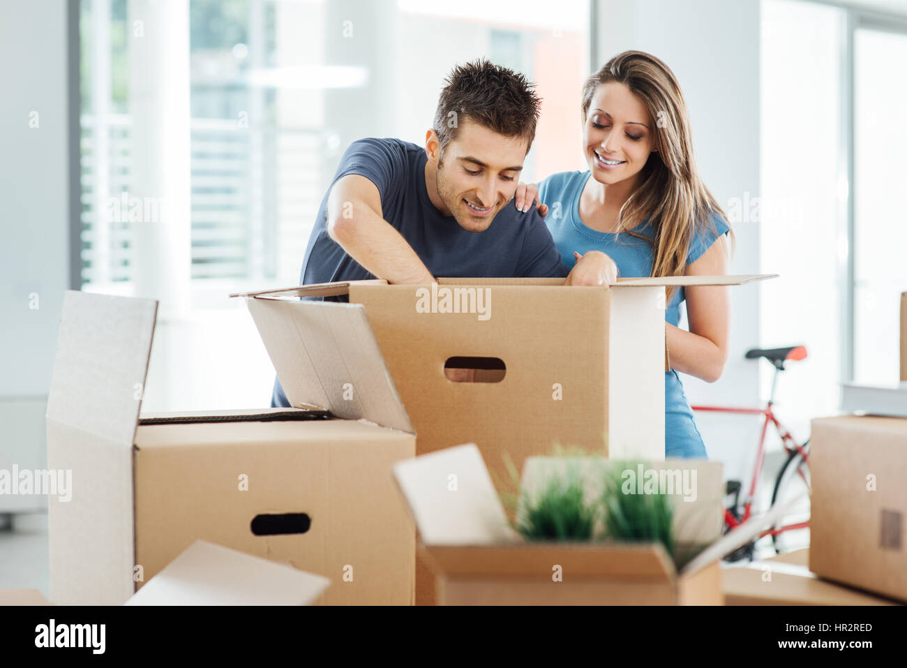 Lächelnd junges Paar Auspacken der Kartons in einem neuen Haus, sucht Objekte in einer großen Kiste auf dem Tisch er Stockfoto