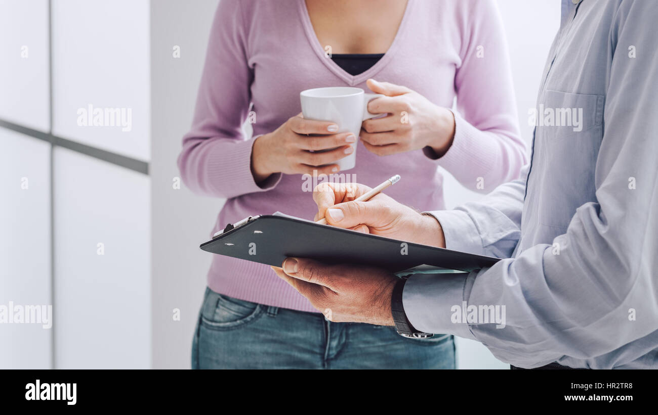 Unternehmen, die Menschen mit einem Briefing während einer Kaffeepause, eine Frau hält eine Tasse Kaffee, ihr Kollege hält eine Zwischenablage und zeigt mit einem p Stockfoto