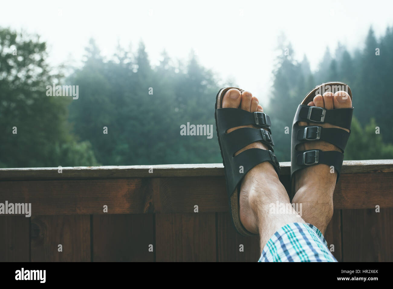 Mann genießt nebligen Morgen am Berg Hotelbalkon, Füße in Leder Pantoffeln gekreuzt Stockfoto