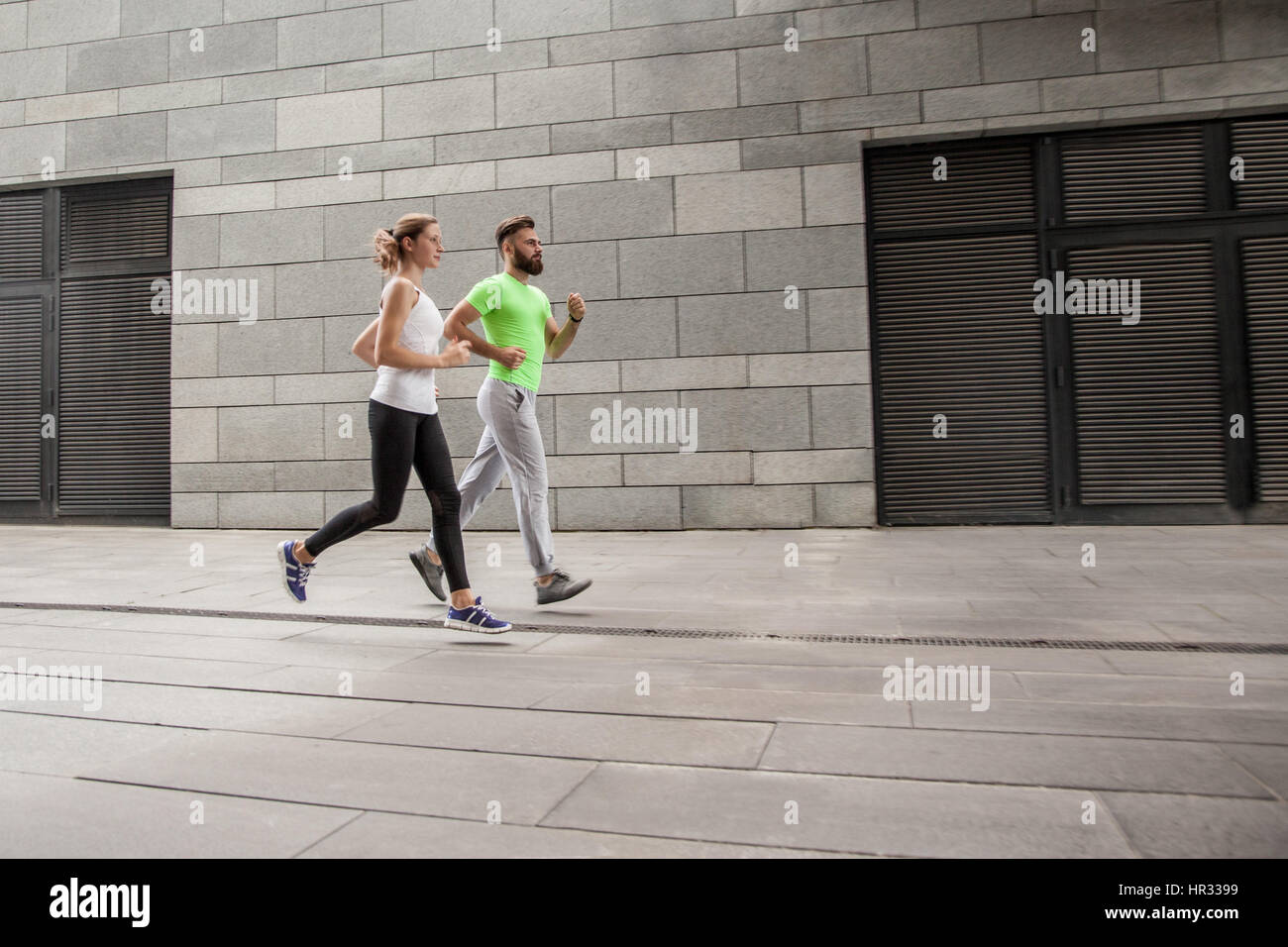 Aktive junge Brautpaar Joggen nebeneinander in einer städtischen Straße während ihr tägliches Workout in einem Gesundheits- und Fitness-Konzept. Sport Watch verwenden. Stockfoto