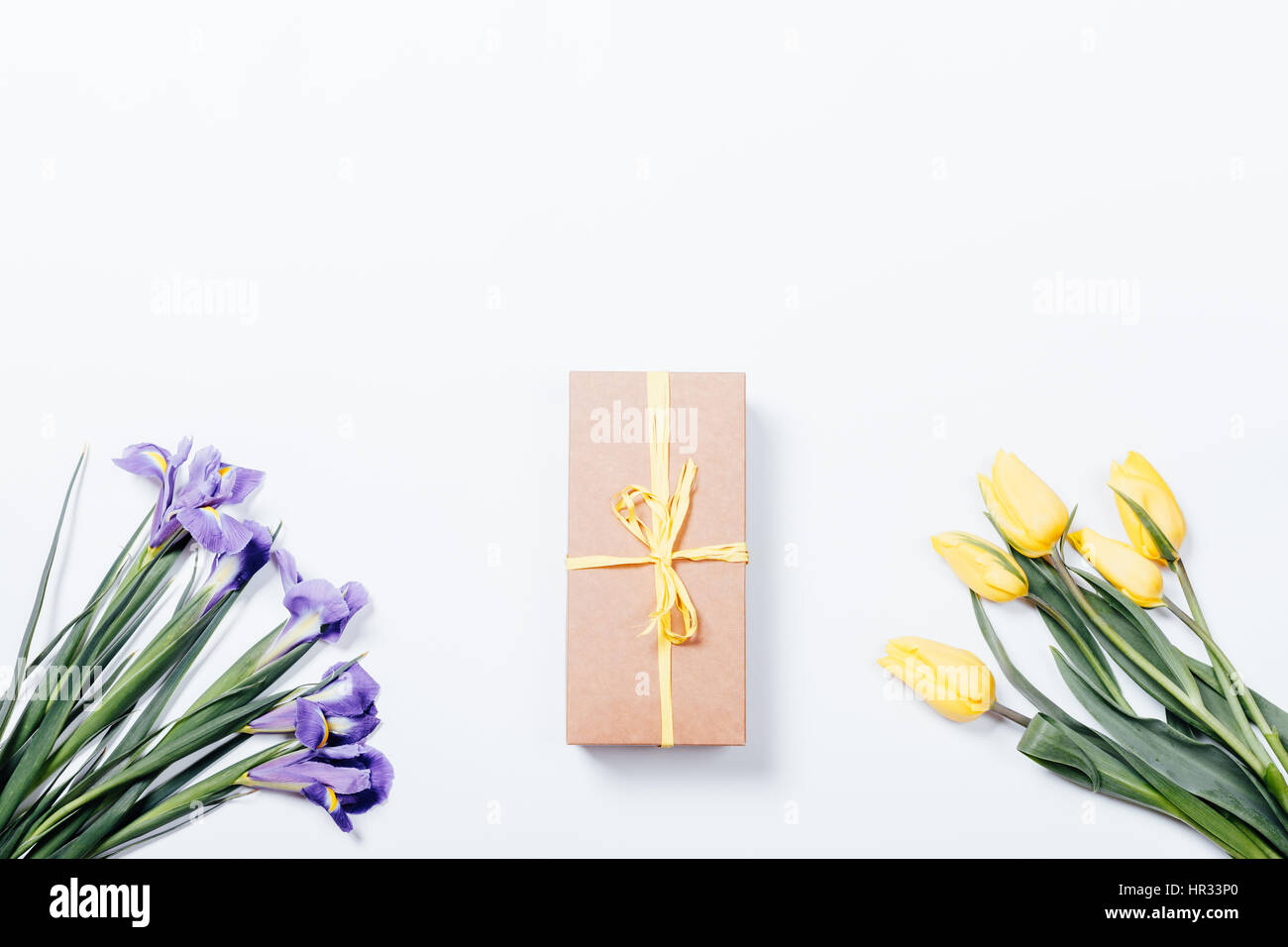 Violette Iris, gelbe Tulpen und Geschenk-Box mit einem Band auf einem weißen Hintergrund, Ansicht von oben Stockfoto