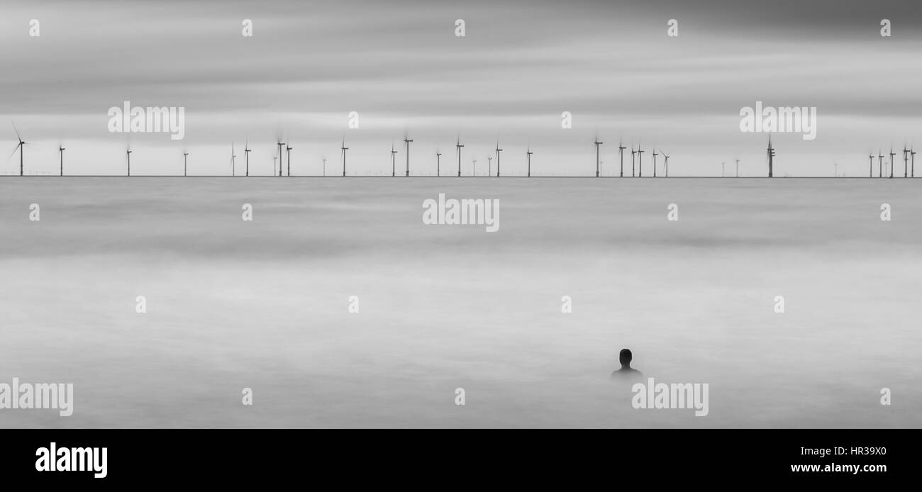 Man von Antony Gormley lebensgroße Statuen von sich selbst (die "Woanders" an der Küste von Sefton ausmachen) beobachtet den Windpark während Terra Stockfoto