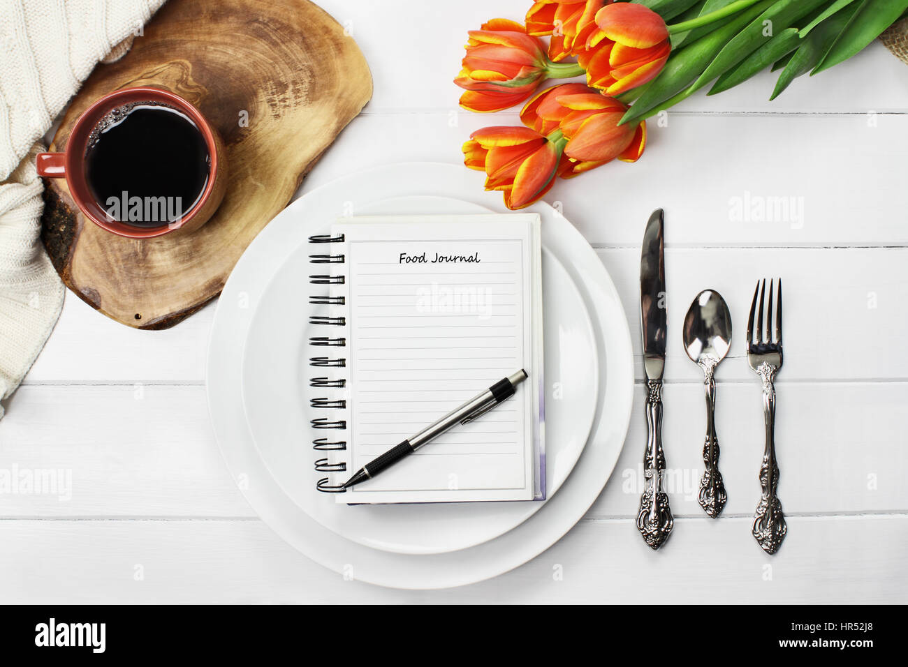 Overhead Schuss ein Ernährungstagebuch über leere Teller mit einer Tasse Kaffee und ein Blumenstrauss Frühling Tulpe über weiße Holz Tischplatte. Flach legen t Stockfoto