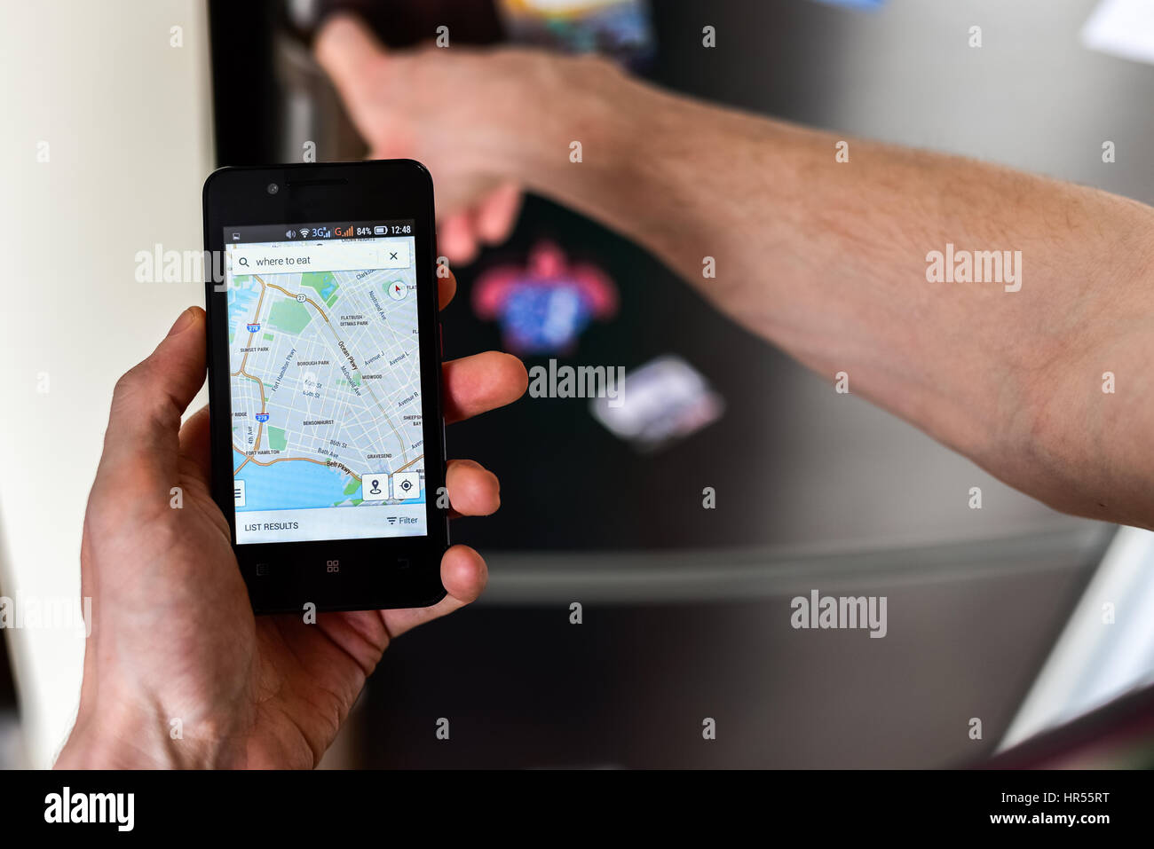 Nahaufnahme einer Person die Hände halten Smartphone Stadtplan auf dem Bildschirm anzeigen und Online-Suche nach Orten auf dieser Karte zu essen. Kühlschrank mit Magneten o Stockfoto