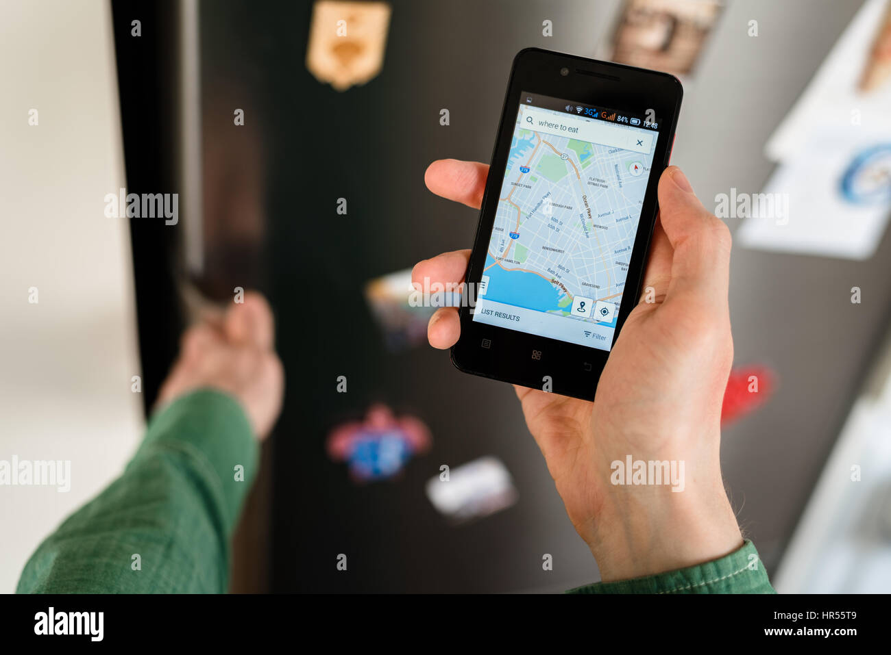 Nahaufnahme einer Person die Hände halten Smartphone Stadtplan auf dem Bildschirm anzeigen und Online-Suche nach Orten auf dieser Karte zu essen. Kühlschrank mit Magneten o Stockfoto