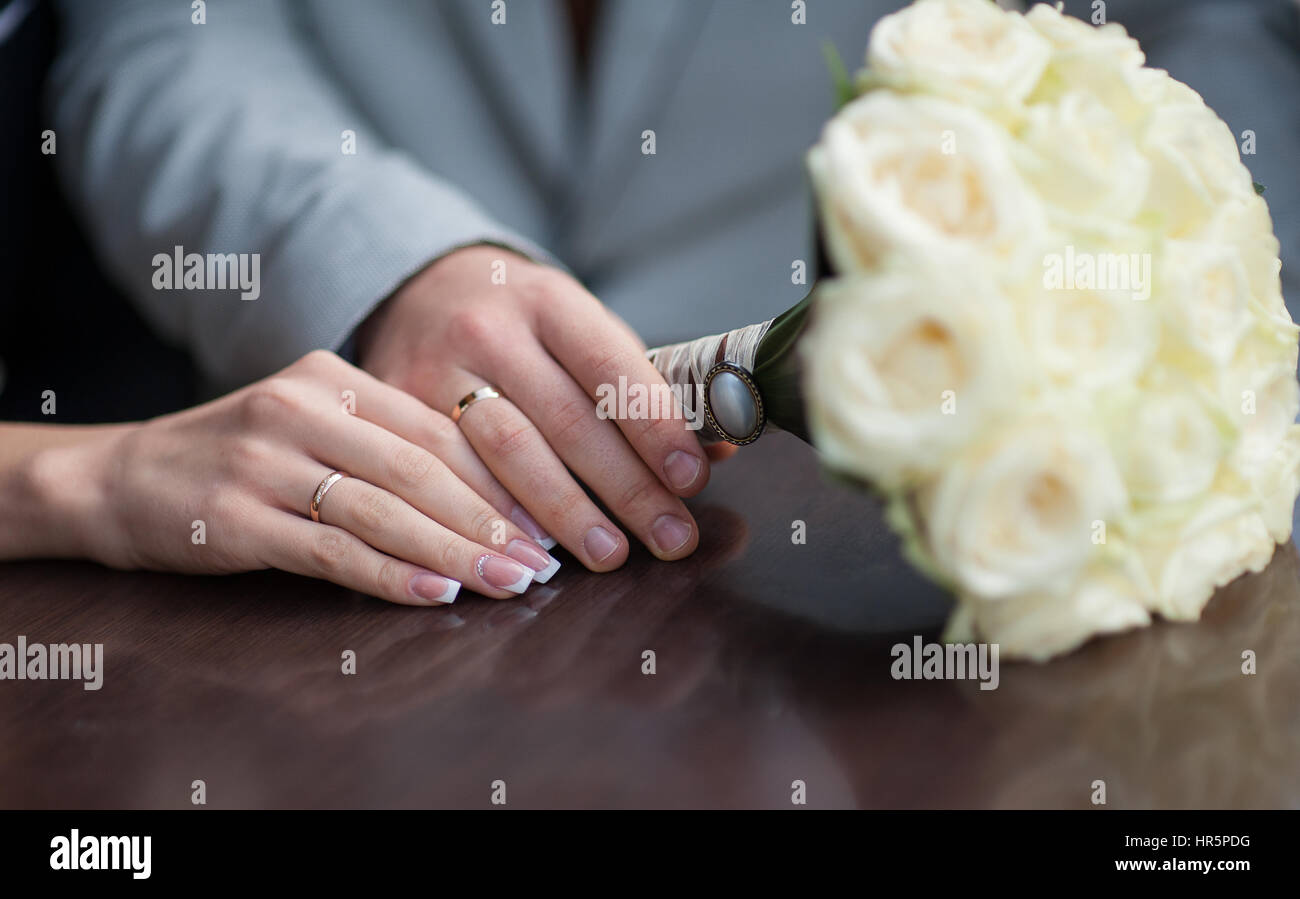 Hände von Braut und Bräutigam mit Eheringe und Strauß Rosen. Stockfoto