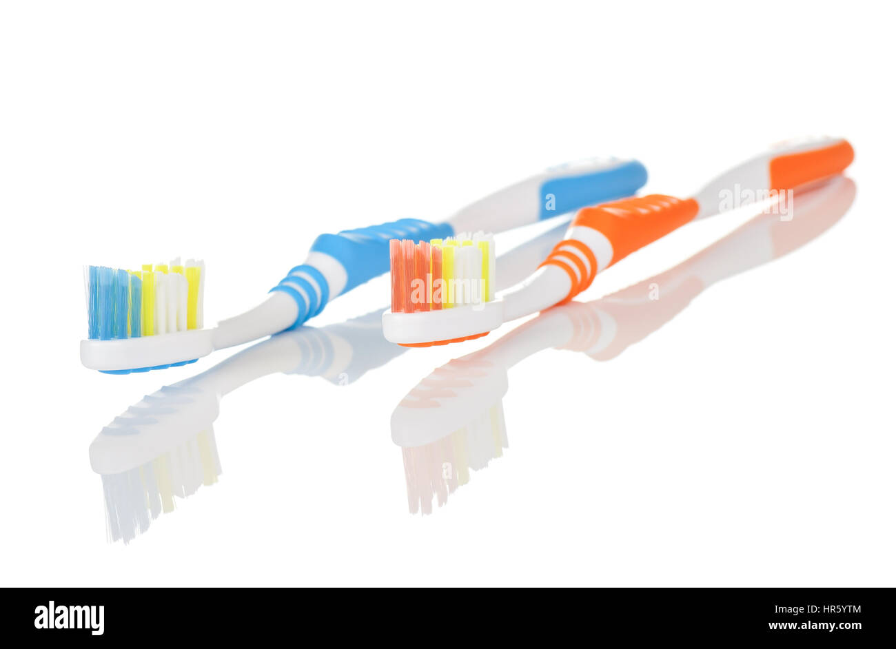 Paar von orangenen und blauen Zahnbürsten auf weißem Hintergrund mit Reflexion Stockfoto