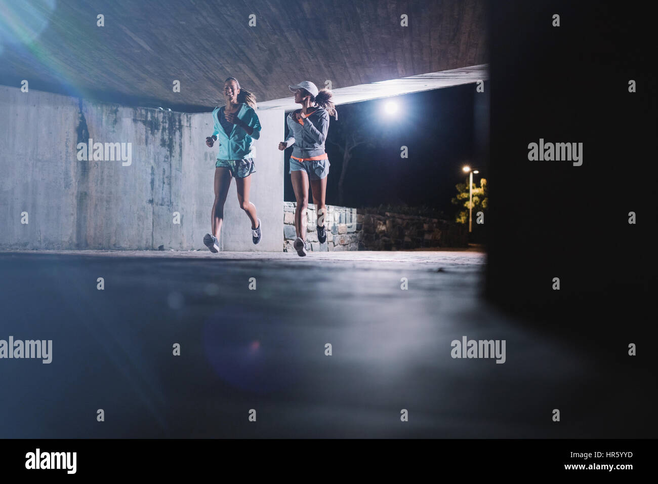 Zwei junge Frauen, die joggen nachts in der Stadt. Läuferinnen, die gemeinsam unter einer Brücke Abend. Stockfoto