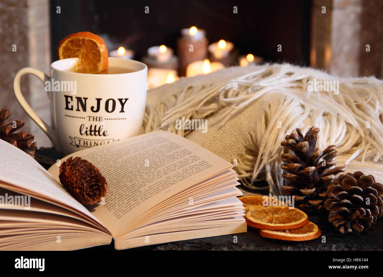 Lesen Sie ein Buch am offenen Kamin in einer gemütlichen Hygge inspiriert englischen Wohnzimmer mit einem heißen Getränk und Decke (werfen) im Herbst / Winter Stockfoto