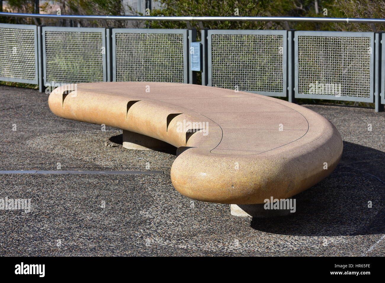 Kurvige Außenbank auf Betondecke vor Metallgeländer. Stockfoto
