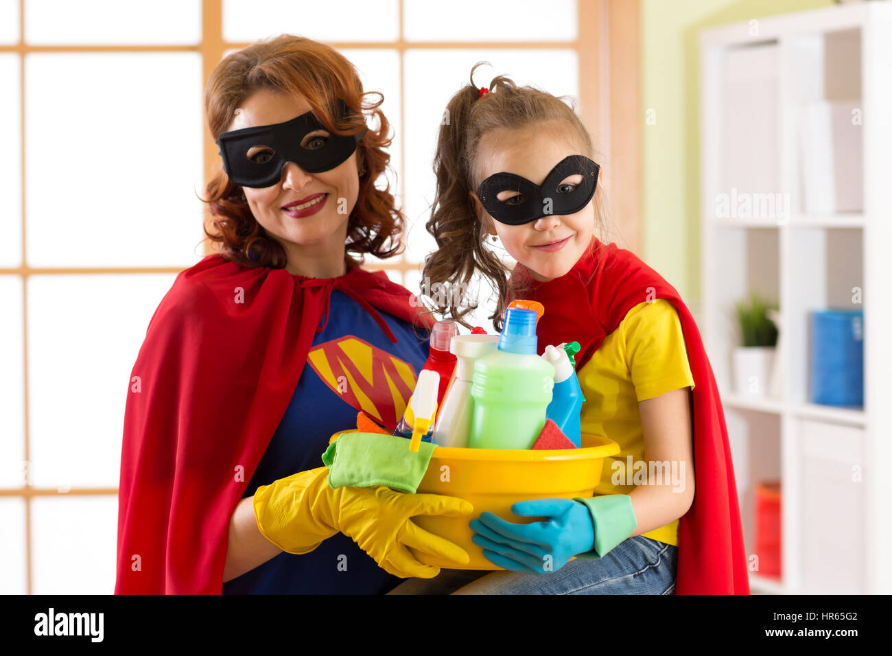 Nettes Kind Mädchen und ihre Mutter machen Hausputz. Kleine Mädchen und Mutter sind in Superman Kostüme gekleidet. Stockfoto