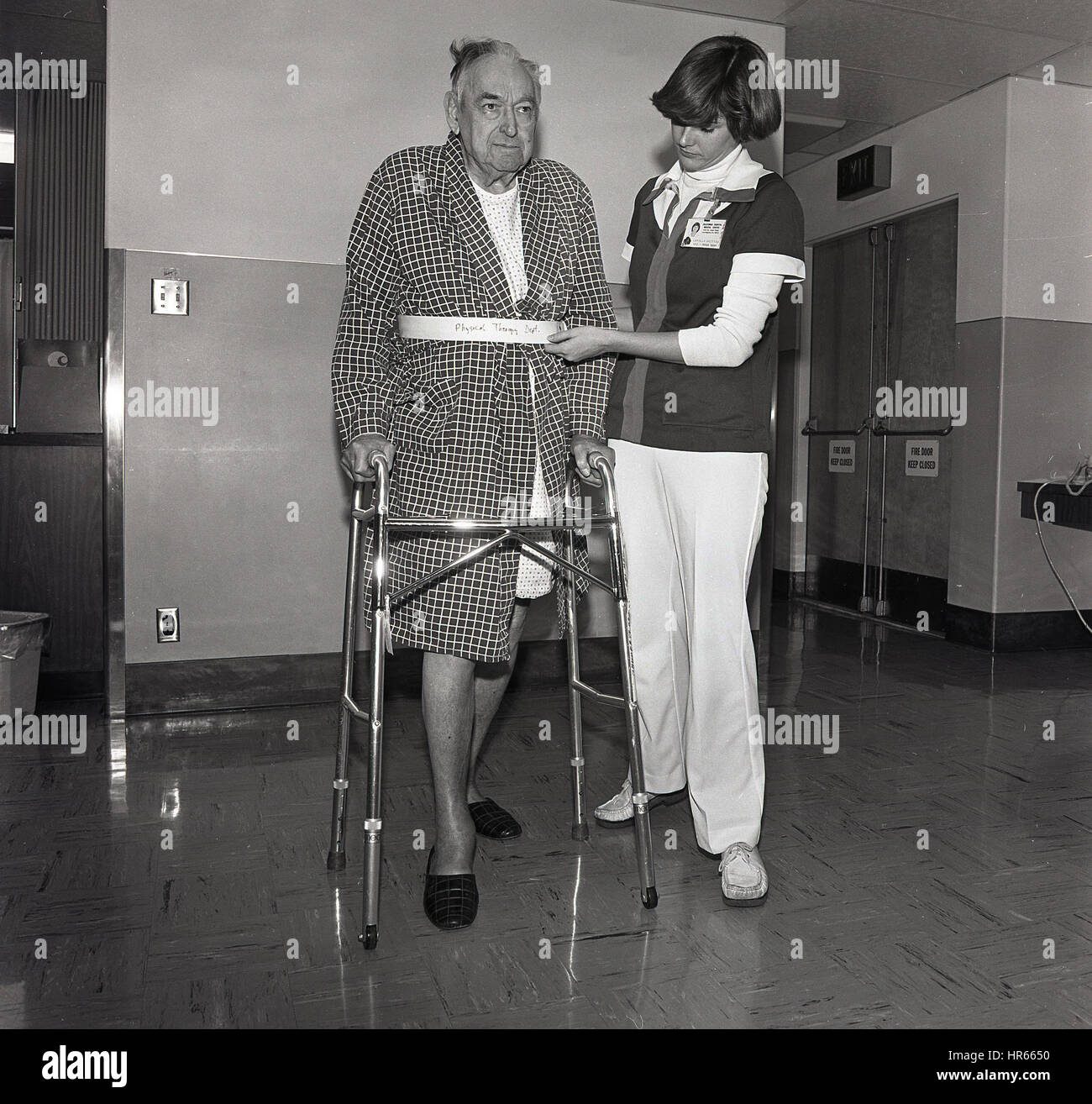1960, historische, Physikalische Therapie, eine weibliche Krankenschwester hilft ein älterer Mann in-Patient in einem Krankenhaus Flur kleine Schritte mit Hilfe eines Metall Zimmer Typ frame seine Bewegung, USA zu unterstützen. Stockfoto