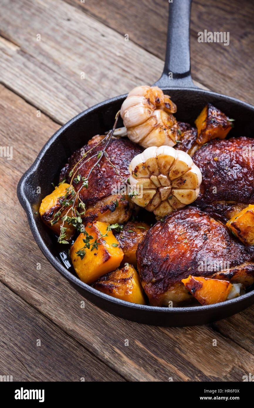 Hausgemachte gebratene Hähnchenschenkel mit mit Butternut, Thymian und Knoblauch in Gusseisen Pfanne auf rustikalen Holztisch Stockfoto