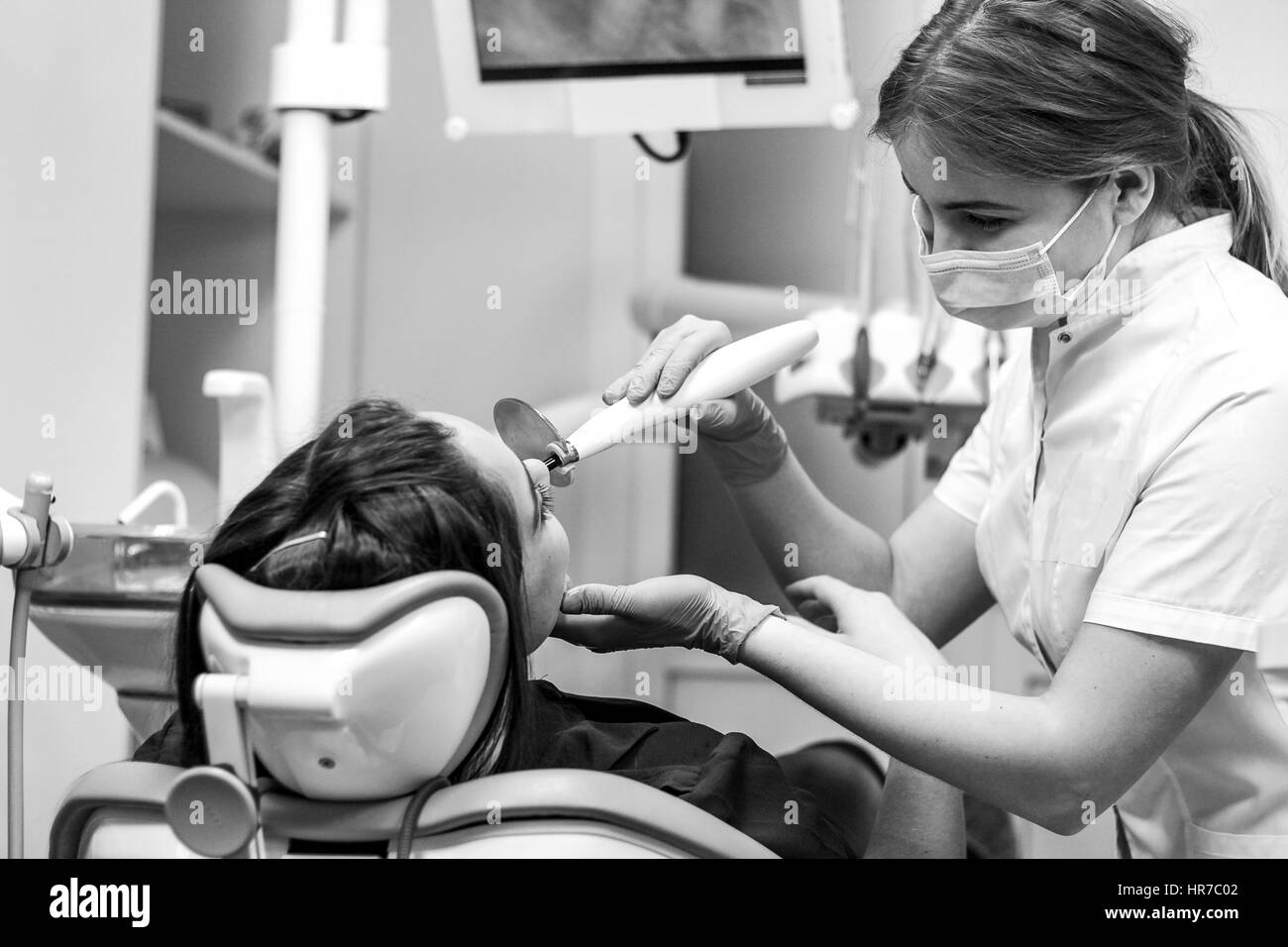 Black And White Nahaufnahme der Patientin beim Zahnarzt machen Zahnfüllungen mit UV-Licht. Arzt lächelt durch Gesichtsmaske Stockfoto