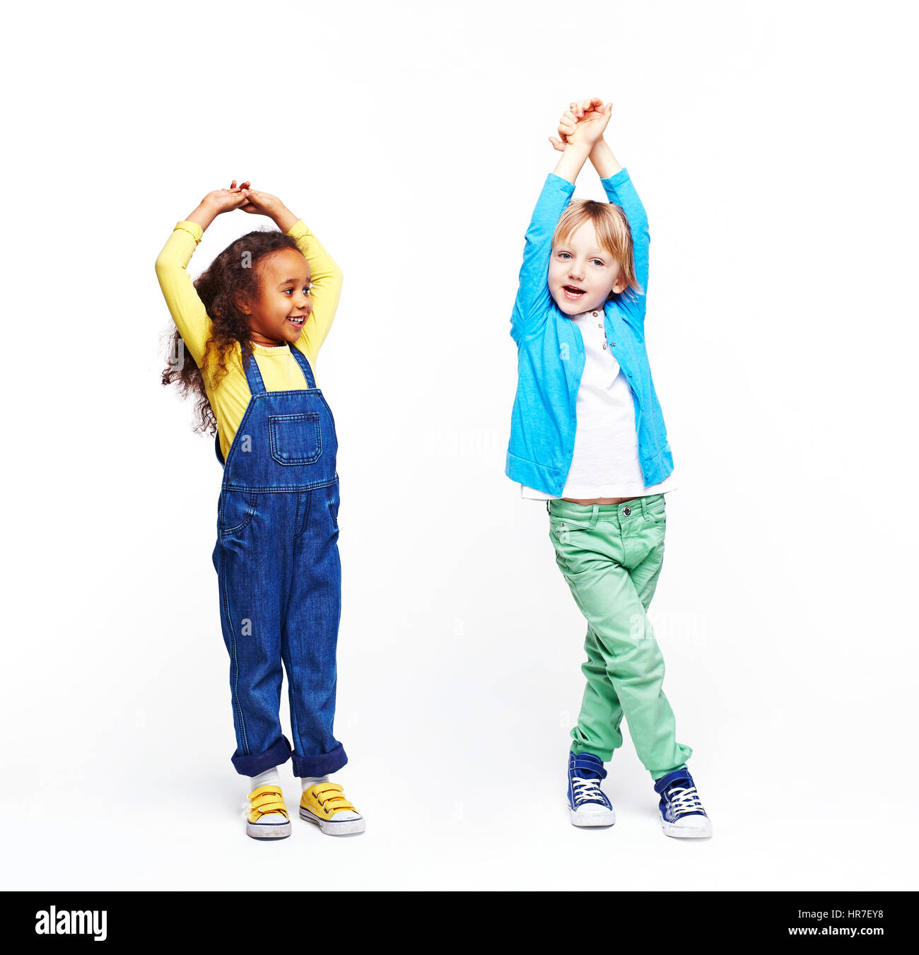 Studioportrait von Kindern vor weißem Hintergrund: volle Stelle erschossen zwei aktive Kinder, afrikanische Mädchen und blonder Junge, lustige Posen mit Händen, tun Stockfoto