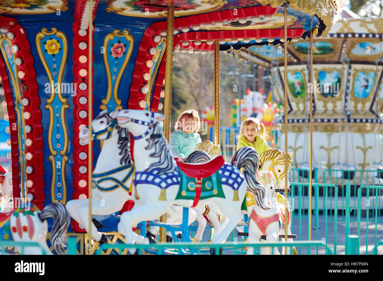 Porträt von lustigen blonden Mädchen mit einem breiten Lächeln Reiten auf bunten Karussell beim Wochenende mit ihrer Familie im park Stockfoto