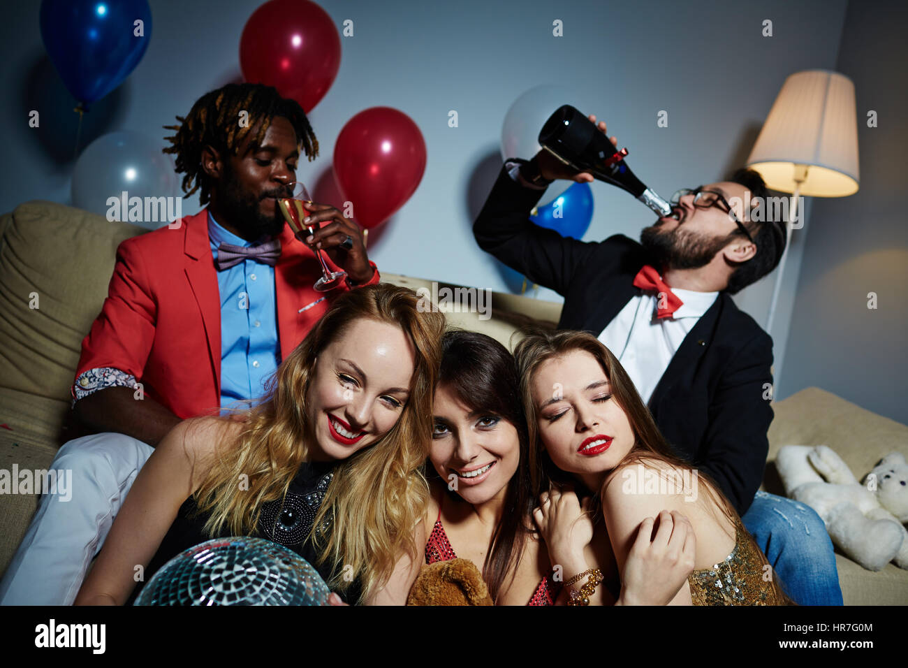 Drei Elegant Frohliche Frauen Sitzen Auf Boden Und Posieren Fur Fotografie Wahrend Ihre Mannlichen Freunde Trinken Champagner Auf Hintergrund Stockfotografie Alamy