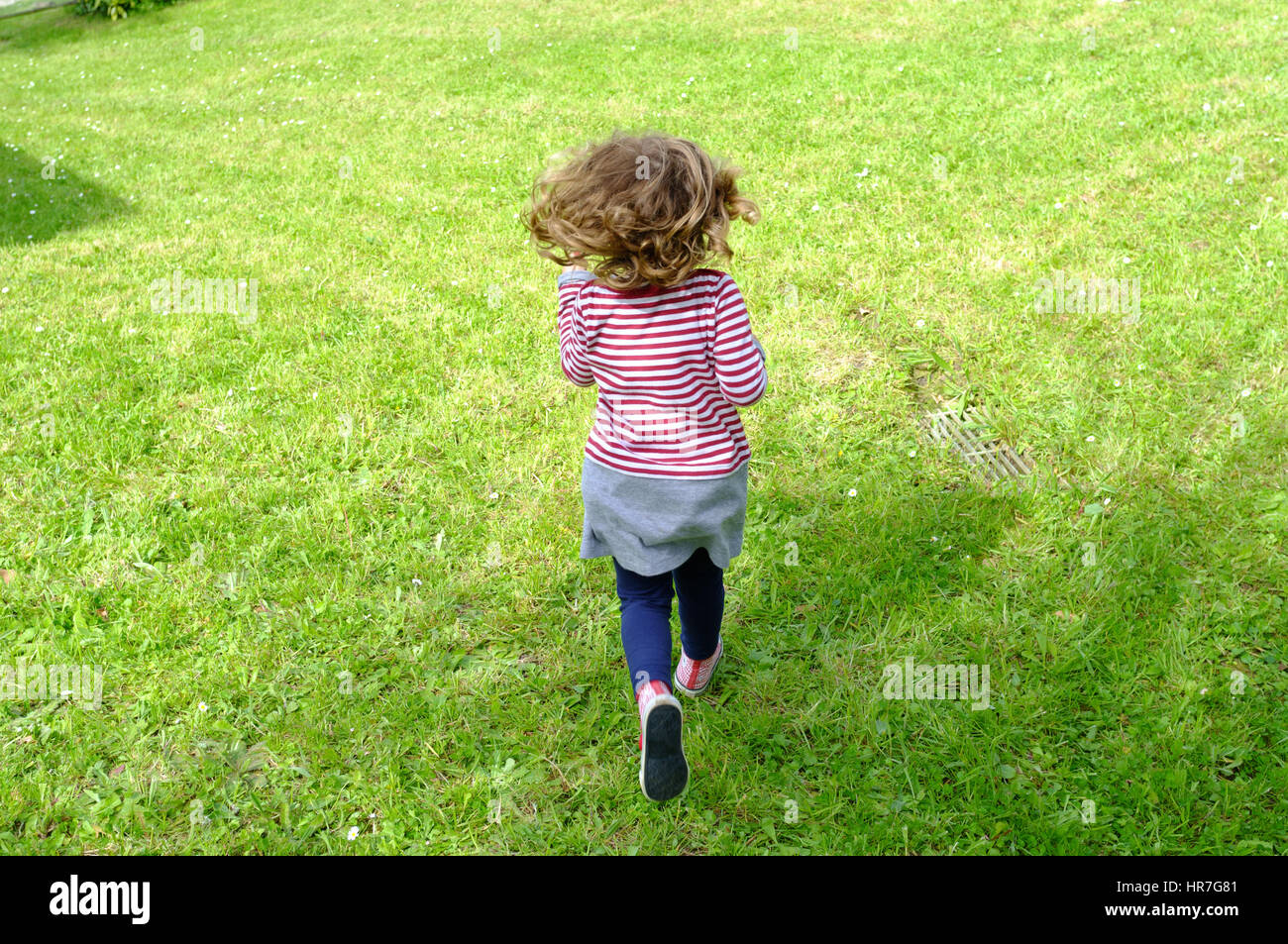 Ein kleines Mädchen in Streifen laufen in einem Garten, Blick von der Rückseite Stockfoto