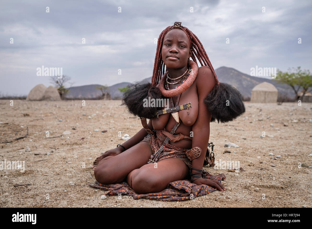 Porträt einer Himba-Frau sitzt auf dem Boden in einem kleinen Dorf. Himbas sind ein Bantu Stamm, wanderten nach heutigen Namibia ein paar Jahrhunderte ist, ein Stockfoto