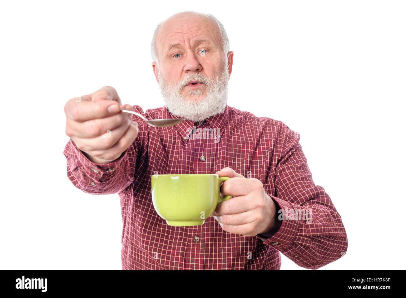 Unbekümmerte senior Mann mit grünen Tasse und Teelöffel, isoliert auf weiss Stockfoto