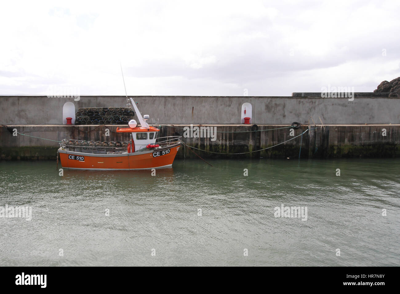 Kleines orangefarbenes Küstenfischboot mit Seil, das am Steinkai im Hafen von Portstewart, County Londonderry, Nordirland, festgemacht ist. Stockfoto