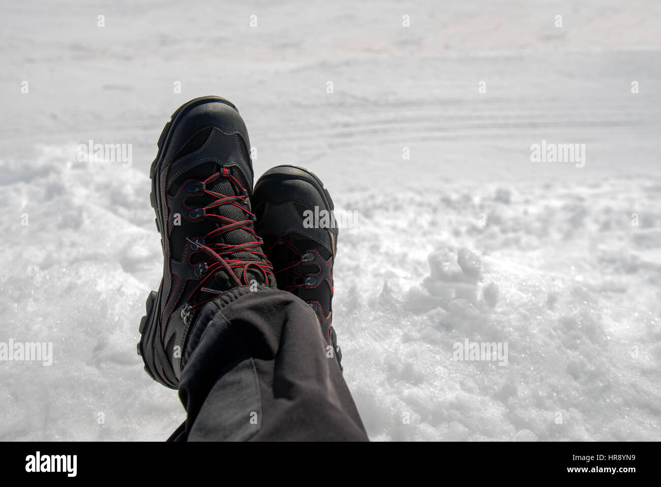 Entspannend auf Schnee, männliche Beine in Stiefeln an hellen Wintertag gekreuzt Stockfoto
