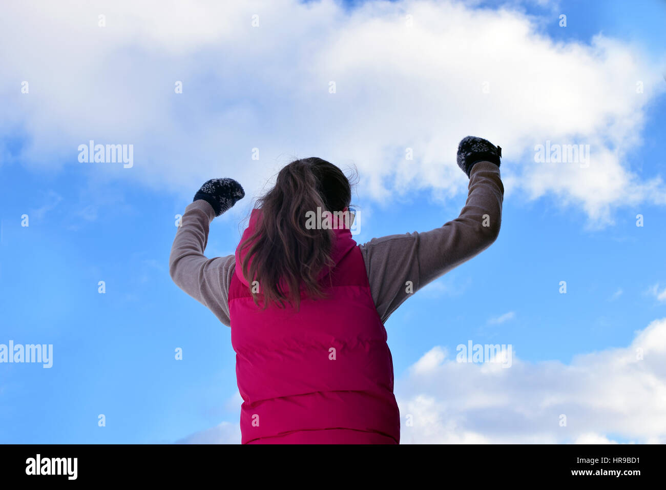 Junge Frau, die Hände unter bewölktem Himmel erhebend. Stockfoto