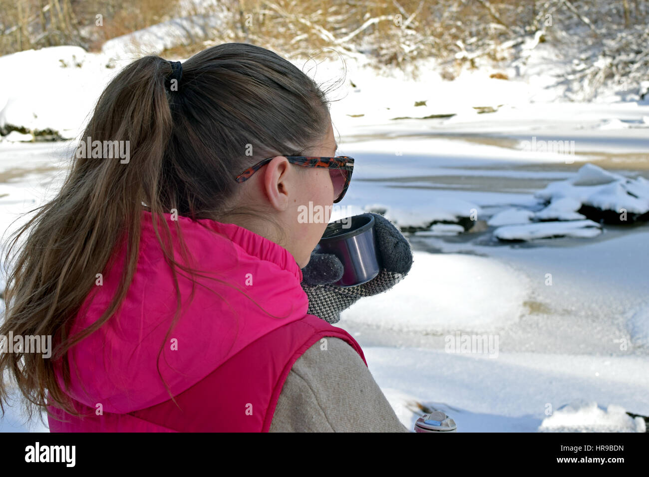 Junge Frau trinken heißen Tee auf Winterwald und gefrorenen Fluss beobachten. Stockfoto