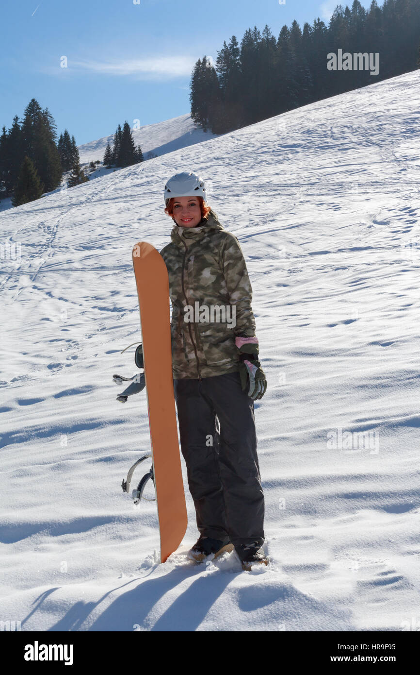 Junge rothaarige Frau mit Helm ist auf der Piste und hat ein Snowboard in der hand Stockfoto