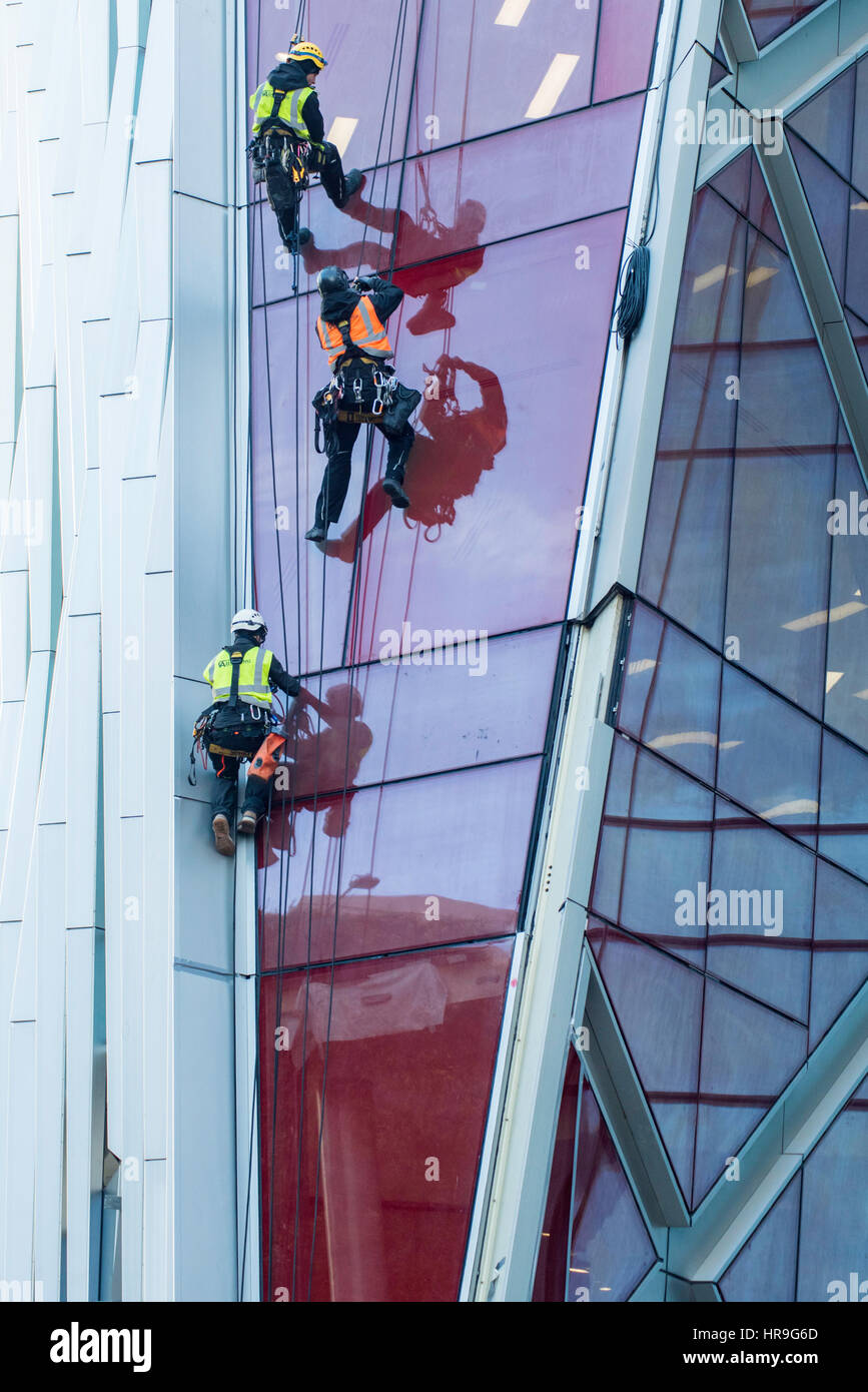 Drei Arbeiter tragen fluoreszierenden Jacken und Geschirre Abseilen an der Seite eines Wolkenkratzers in London. Stockfoto