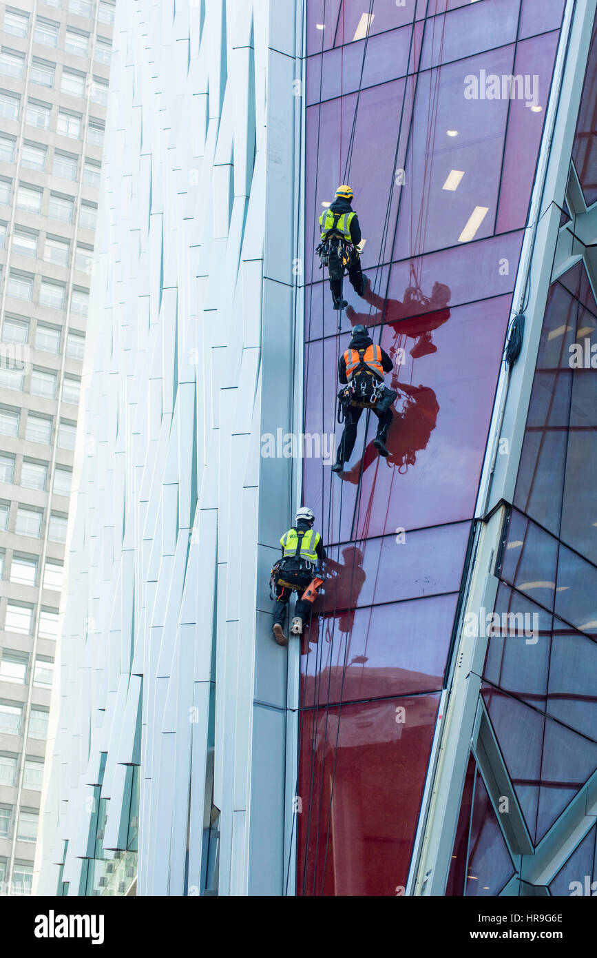 Drei Arbeiter tragen fluoreszierenden Jacken und Geschirre Abseilen an der Seite eines Wolkenkratzers in London. Stockfoto