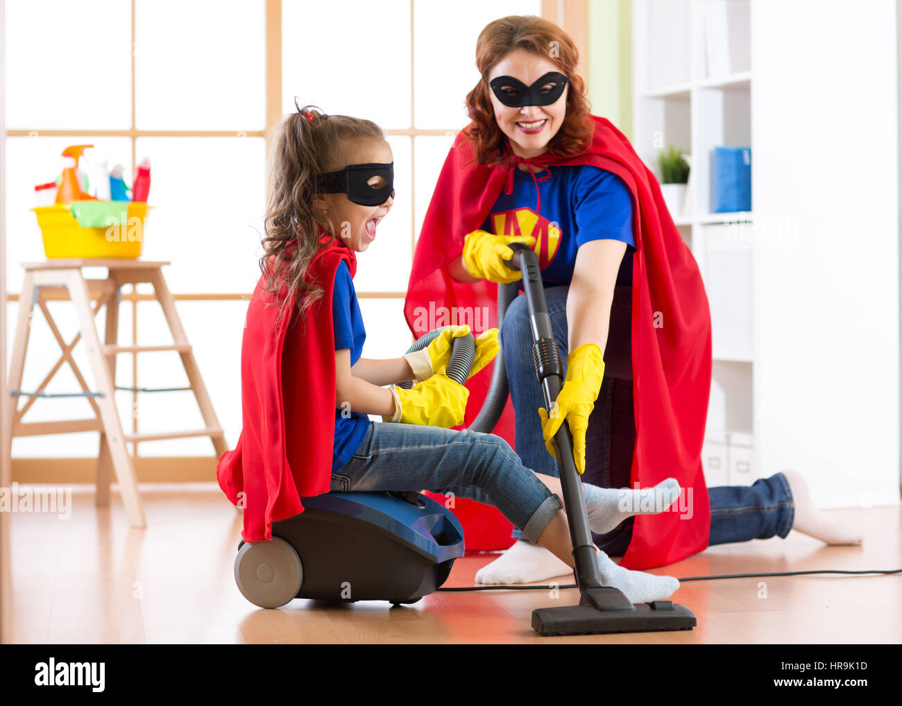 Kind Mädchen und Mutter weared Superheld Kostüme. Niedlichen Helfer Kind und Frau Reinigungsraum machen und Spaß haben. Stockfoto