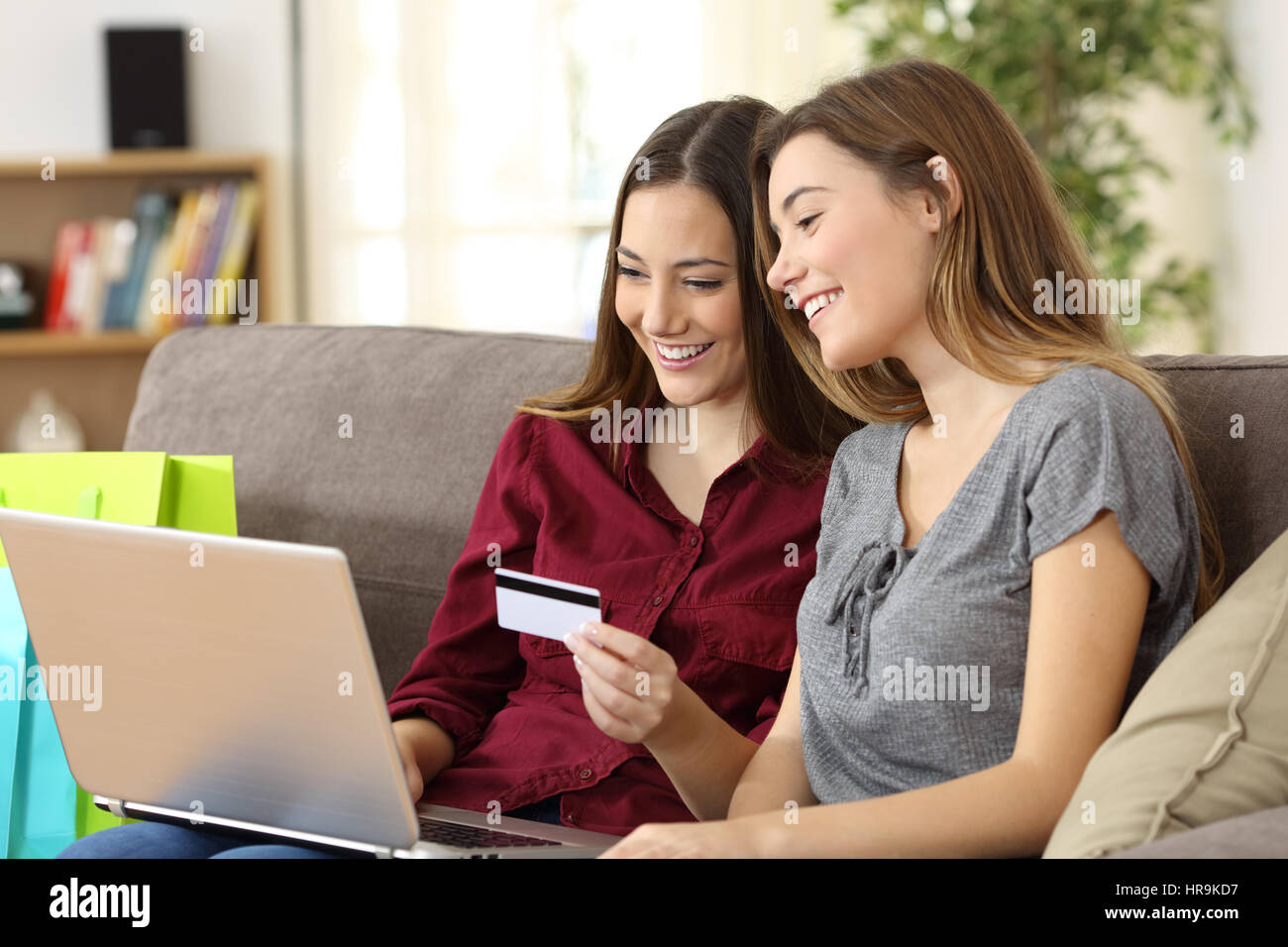 Zwei glückliche Mitbewohner zusammen kaufen online mit Kreditkarte und ein Laptop sitzen auf einem Sofa zu Hause mit einem heimeligen Hintergrund Stockfoto